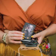 Kobieta trzyma talię kart, jedną z nich jest koło fortuny tarot.