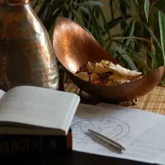 Na stole leży otwarta księga "Astrologie", obok wykresy, długopis i miedziana misa z suszonymi kwiatami. Umiarkowanie tarot uczucia.