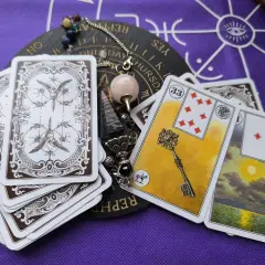 Odkryj znaczenie kart Lenormand. Na stole leżą karty, pendel i talizmany, gotowe do wróżenia.