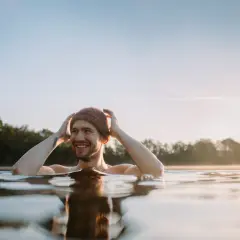 Uśmiechnięty mężczyzna w czapce zanurzony w wodzie, czuje się jak po zaawansowanym wim hof oddychanie poziom 2.