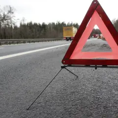 Trójkąt ostrzegawczy na poboczu drogi, zapowiadający 3 mieczy pozytywnie. W tle ciężarówka i inne pojazdy.