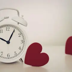 Biały budzik i dwa czerwone serca. Czas na miłość, jak w tarocie, gdzie słońce symbolizuje radość i spełnienie.