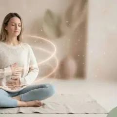 Kobieta w pozycji medytacyjnej, z dłońmi na brzuchu, otoczona świetlistymi kręgami. Idealna chwila na medytację 5 minut.