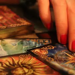 Dłoń z czerwonymi paznokciami nad kartami tarota. Widoczna karta z gwiazdą i znaki zodiaku, sugerująca tarot ryby miesięczny.