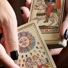 Dłonie trzymają karty tarota, w tym Słońce i rycerza na koniu. Sprawdź, czy tarot online, który się sprawdza, pomoże Ci odkryć przyszłość.