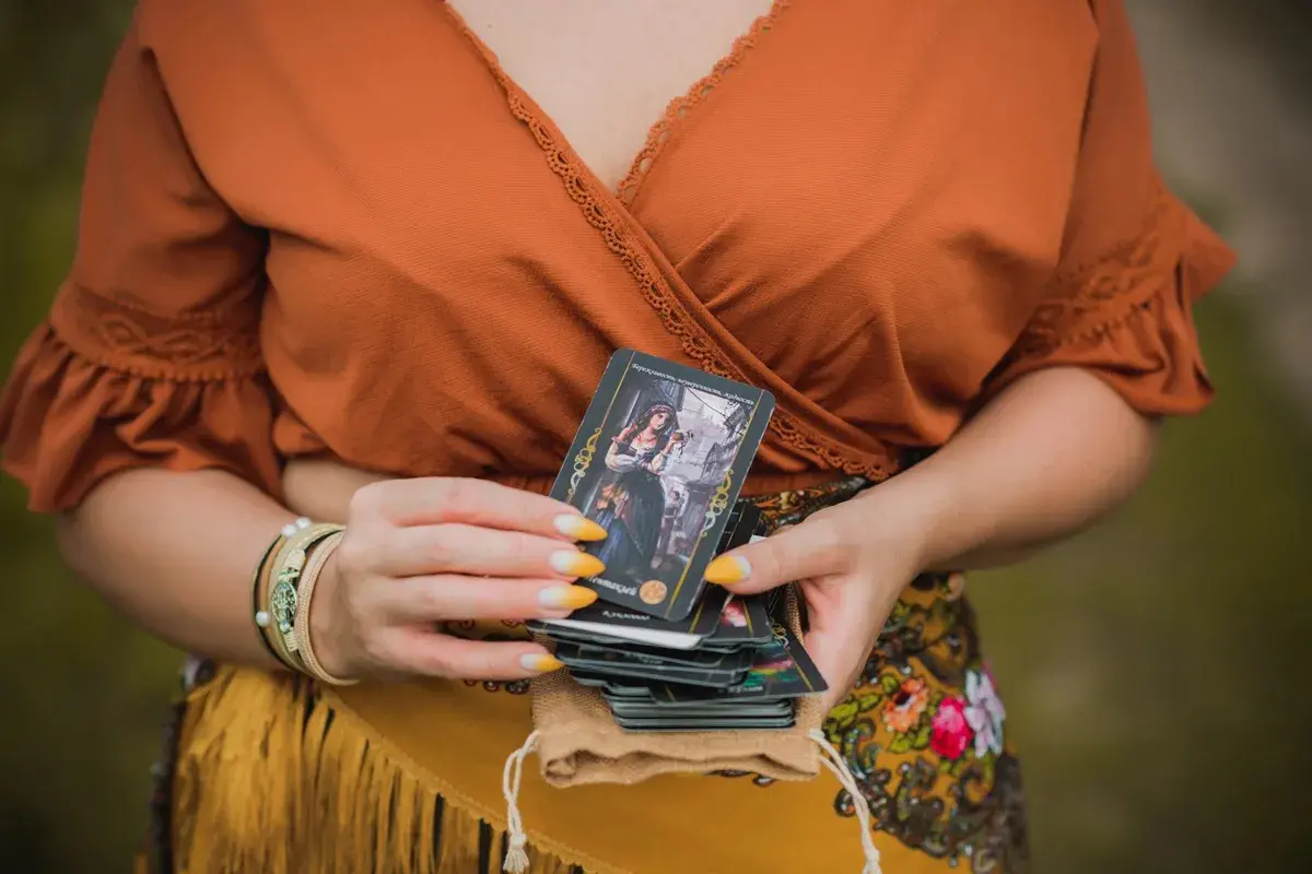 Kobieta trzyma talię kart, jedną z nich jest koło fortuny tarot.