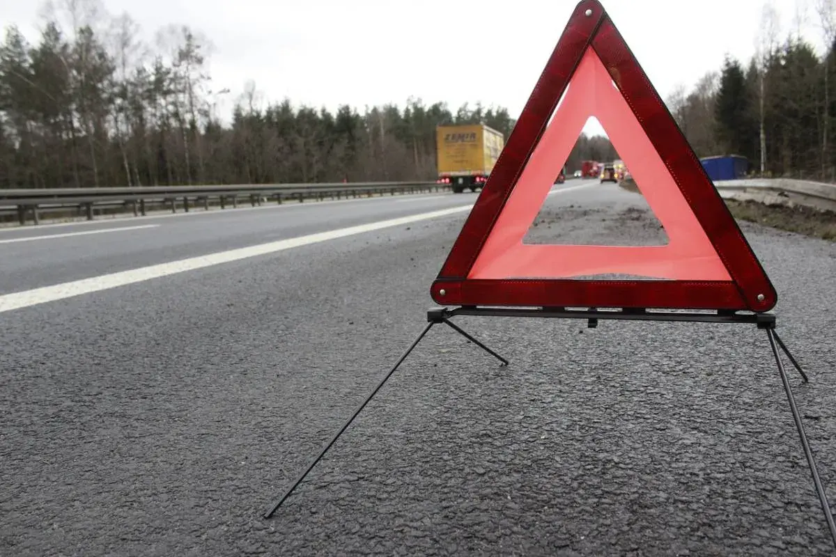 Trójkąt ostrzegawczy na poboczu drogi, zapowiadający 3 mieczy pozytywnie. W tle ciężarówka i inne pojazdy.