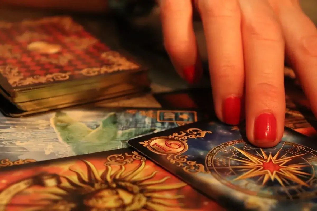 Dłoń z czerwonymi paznokciami nad kartami tarota. Widoczna karta z gwiazdą i znaki zodiaku, sugerująca tarot ryby miesięczny.