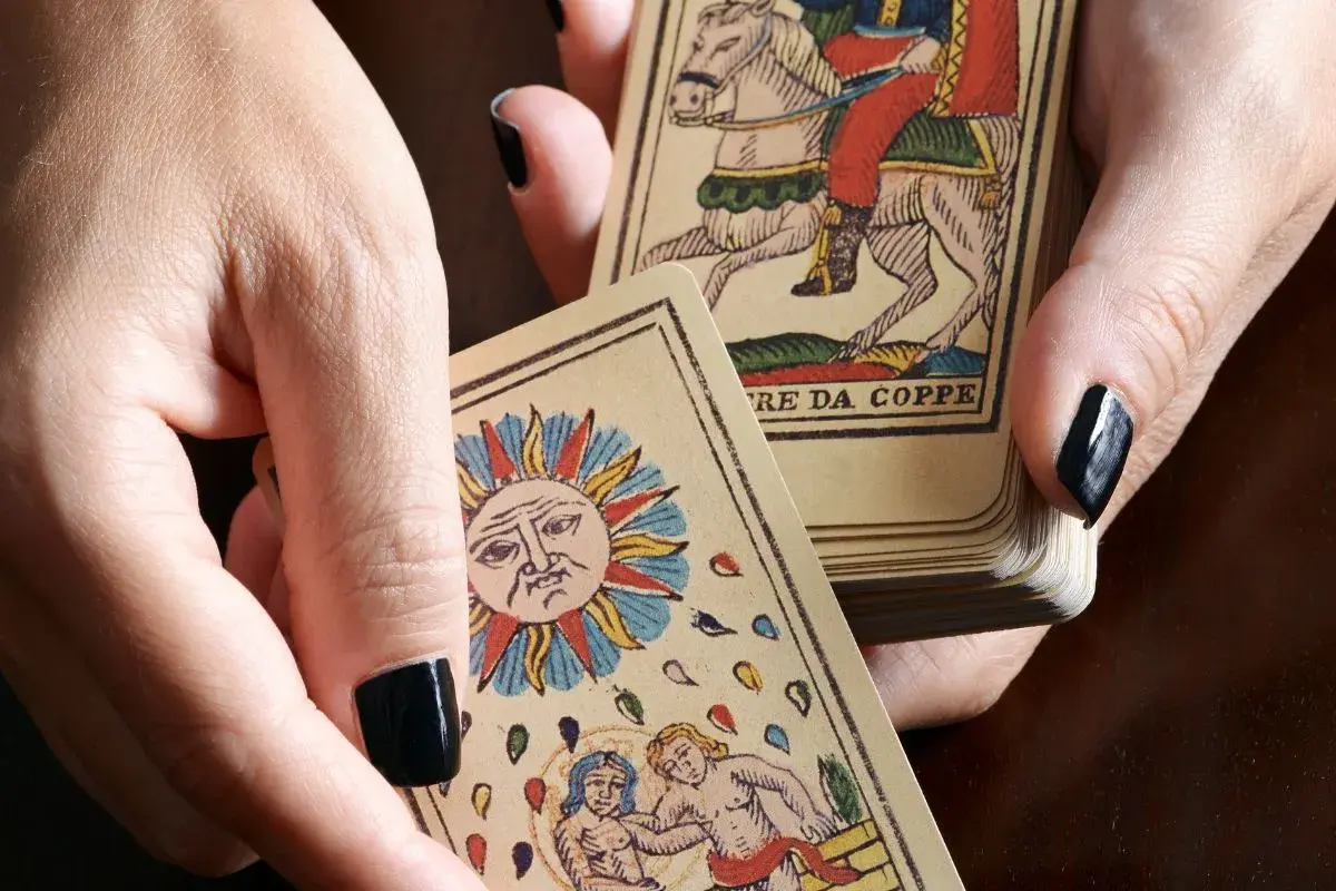 Dłonie trzymają karty tarota, w tym Słońce i rycerza na koniu. Sprawdź, czy tarot online, który się sprawdza, pomoże Ci odkryć przyszłość.
