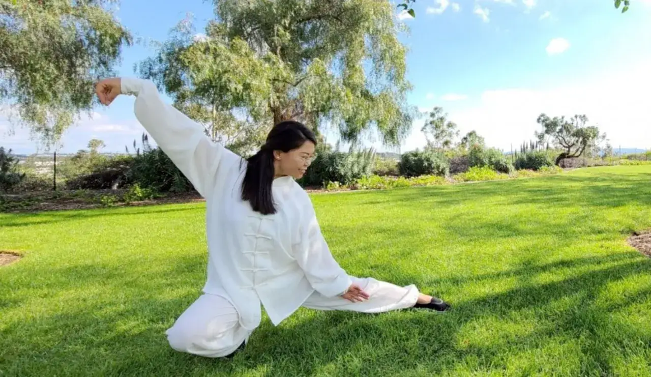 Kobieta w białym stroju ćwiczy qigong na trawie. To starożytna chińska sztuka ruchu i oddechu.